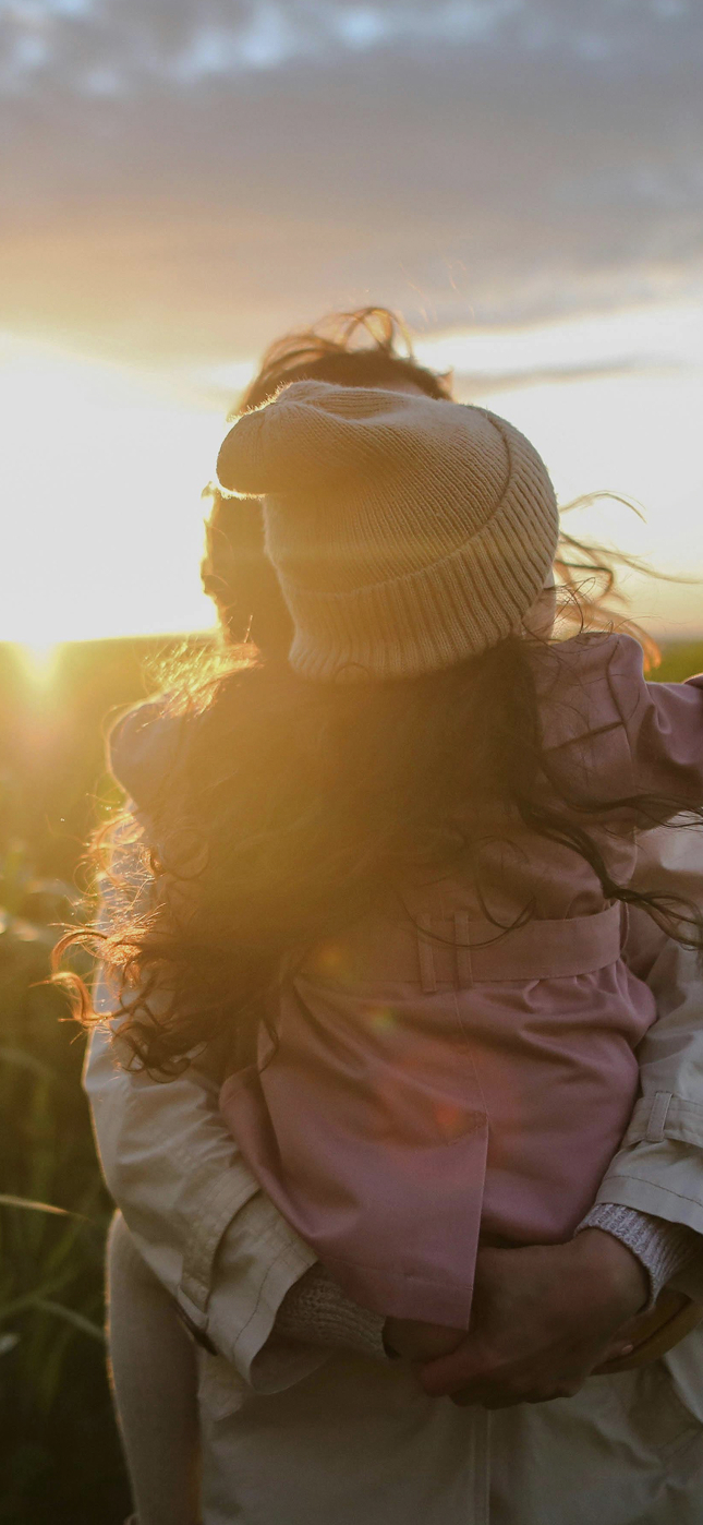 Adult holding child in a corn field at sunset.